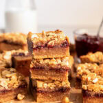 stack of three peanut butter jelly bars in front of more bars and glass milk bottle.