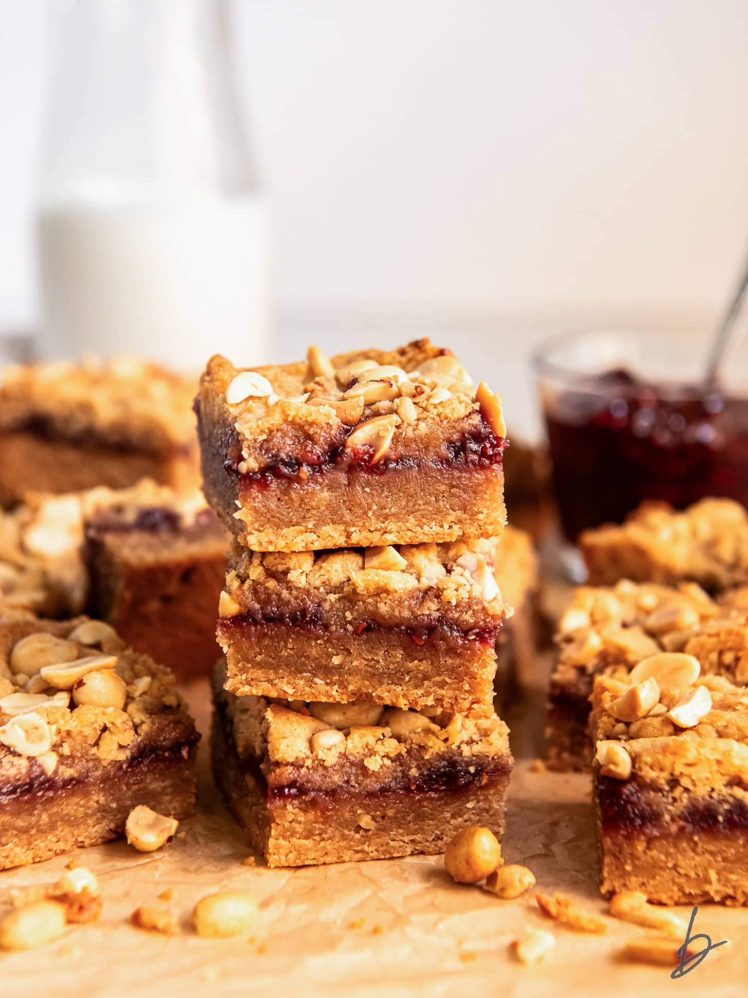 stack of three peanut butter jelly bars in front of more bars and glass milk bottle.