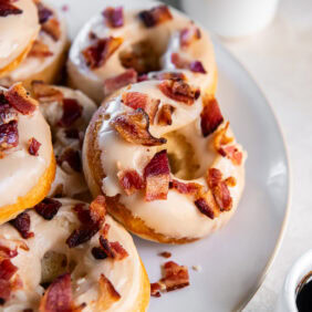 Baked maple bacon donuts on a white plate served with coffee.