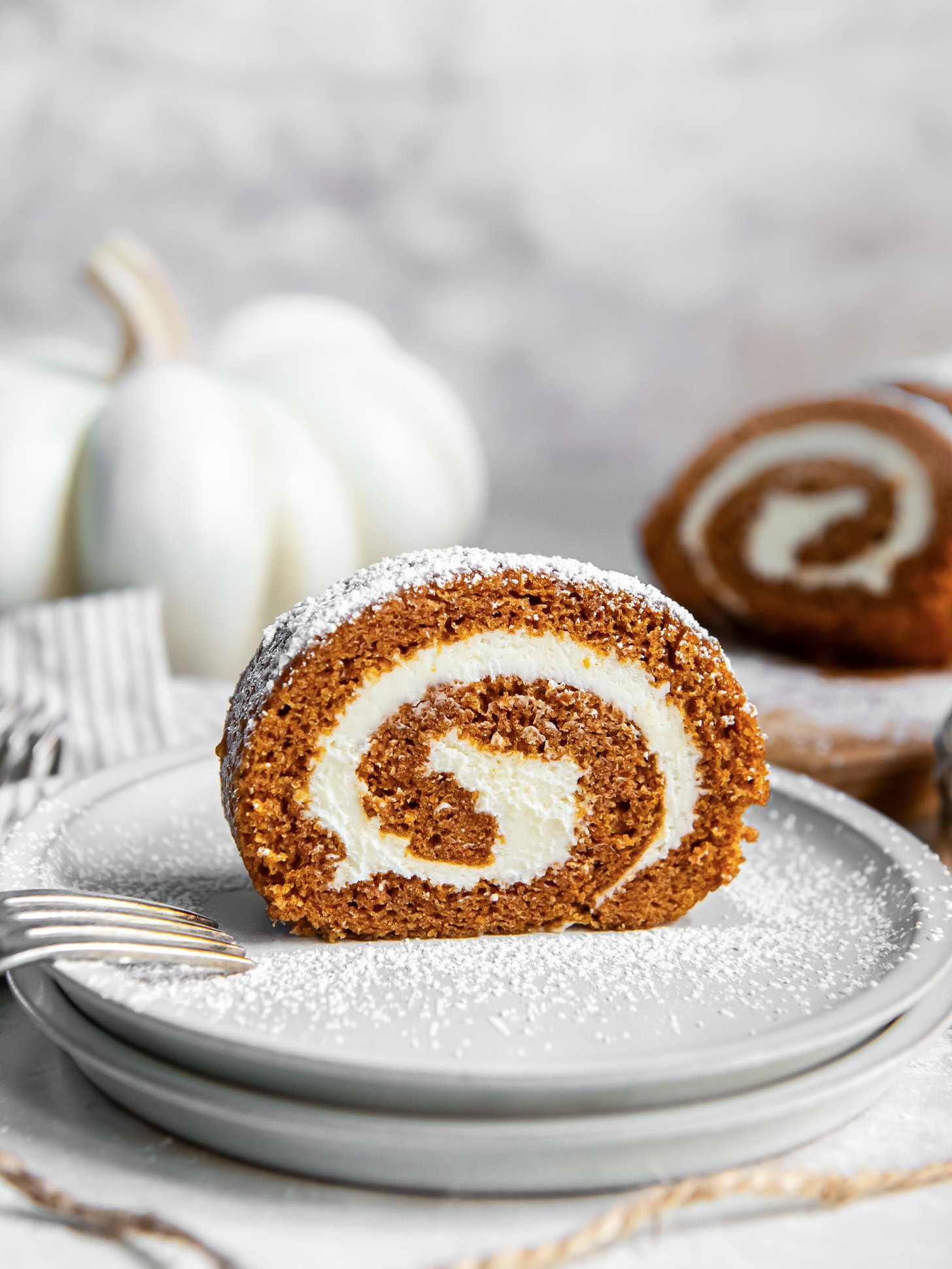 Slice of pumpkin roll cake on a white plate in front of a white pumpkin.
