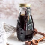 A jar filled with homemade vanilla extract sitting on a white plate near small wooden spoons.