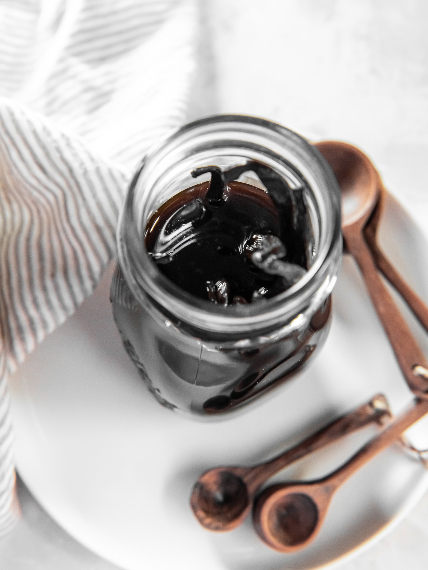Vanilla bean pods in a jar with vodka sitting on a white plate.