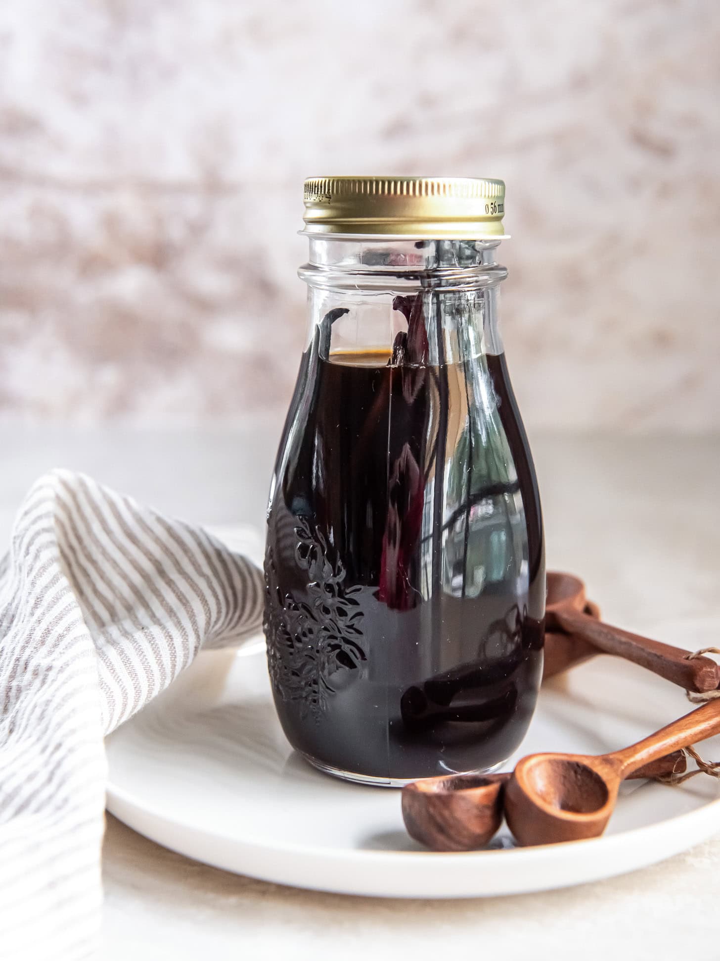 A jar filled with homemade vanilla extract sitting on a white plate near small wooden spoons.