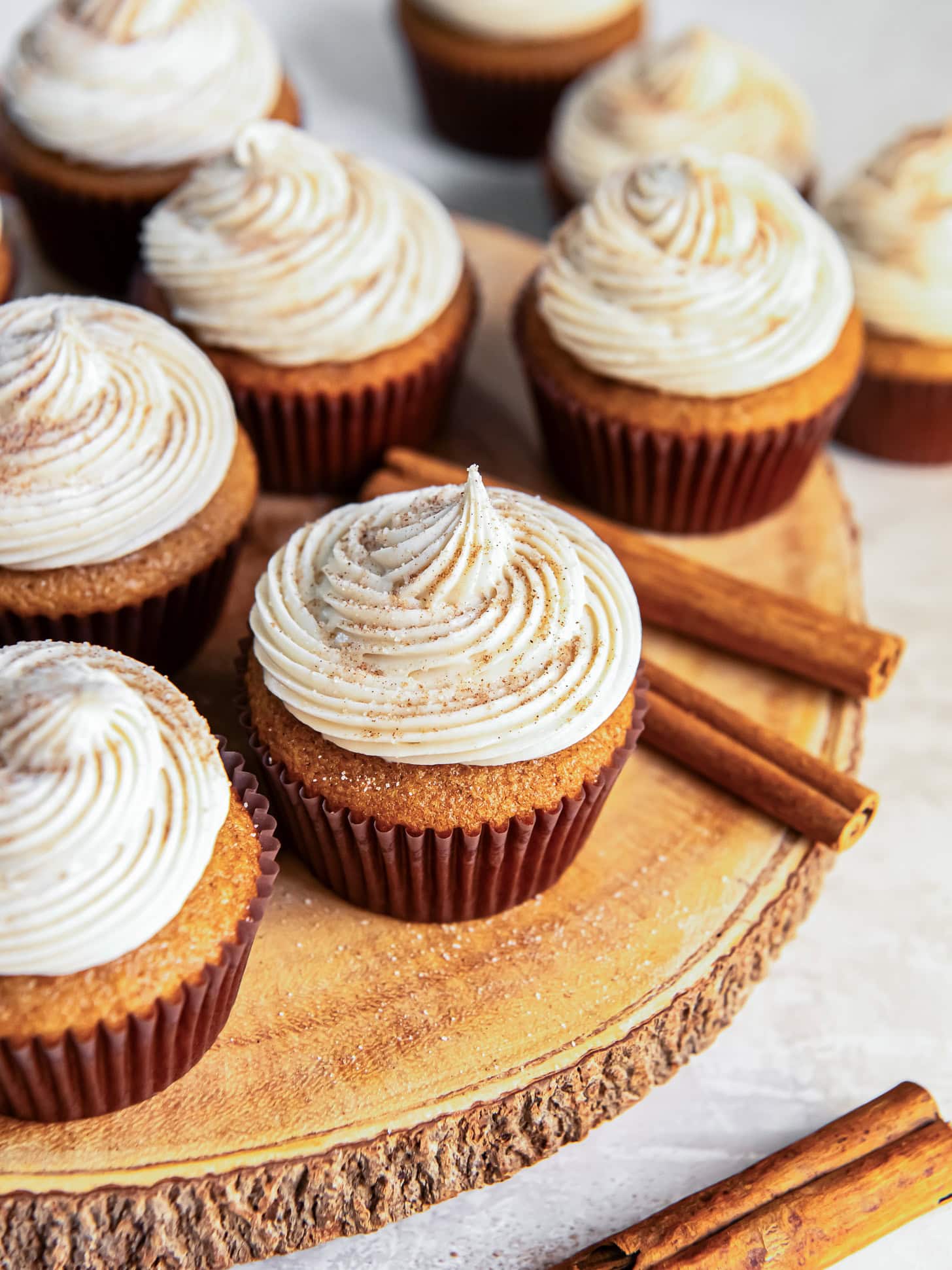 Frosted cupcakes on a wooden board near cinnamon sticks.