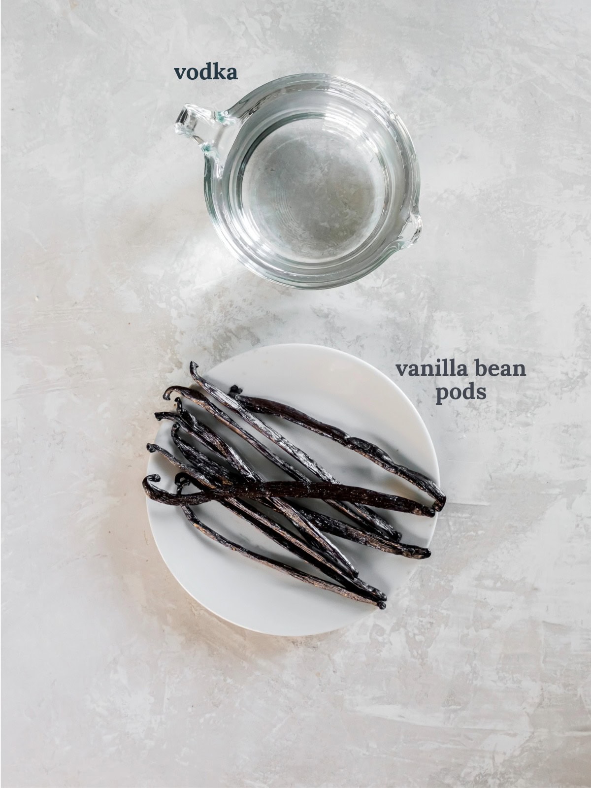 Vanilla bean pods on a white plate near a glass of water.