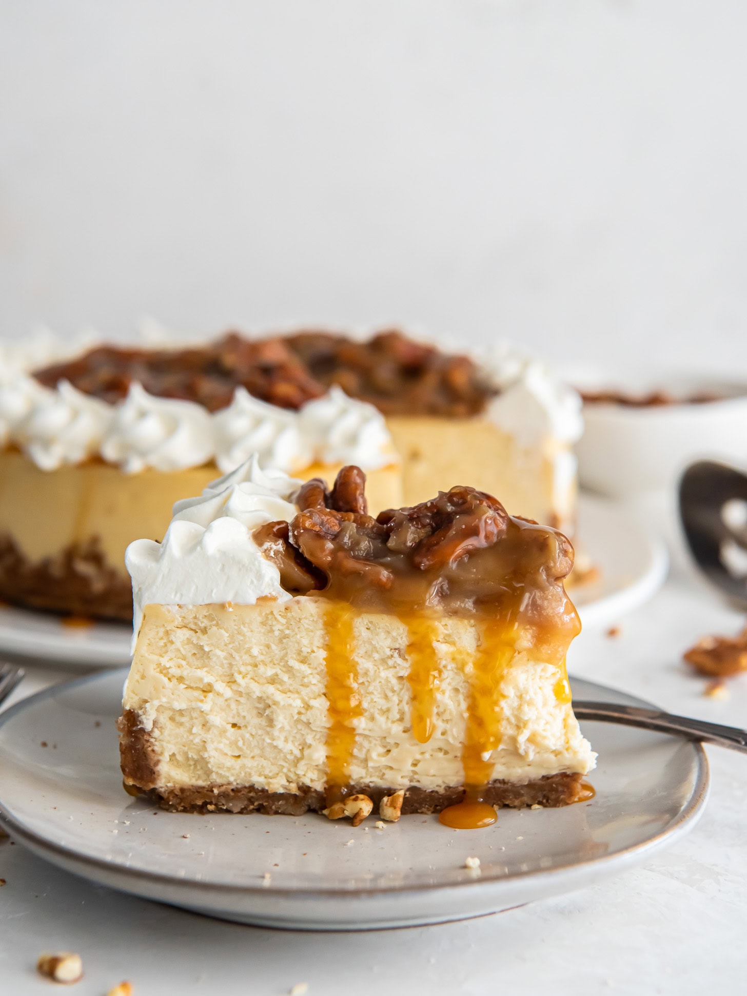 Slice of pecan praline cheesecake on a plate near the whole cheesecake.