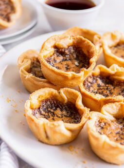 Canadian butter tarts stacked on a white plate served with coffee.