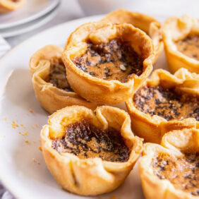 Canadian butter tarts stacked on a white plate served with coffee.