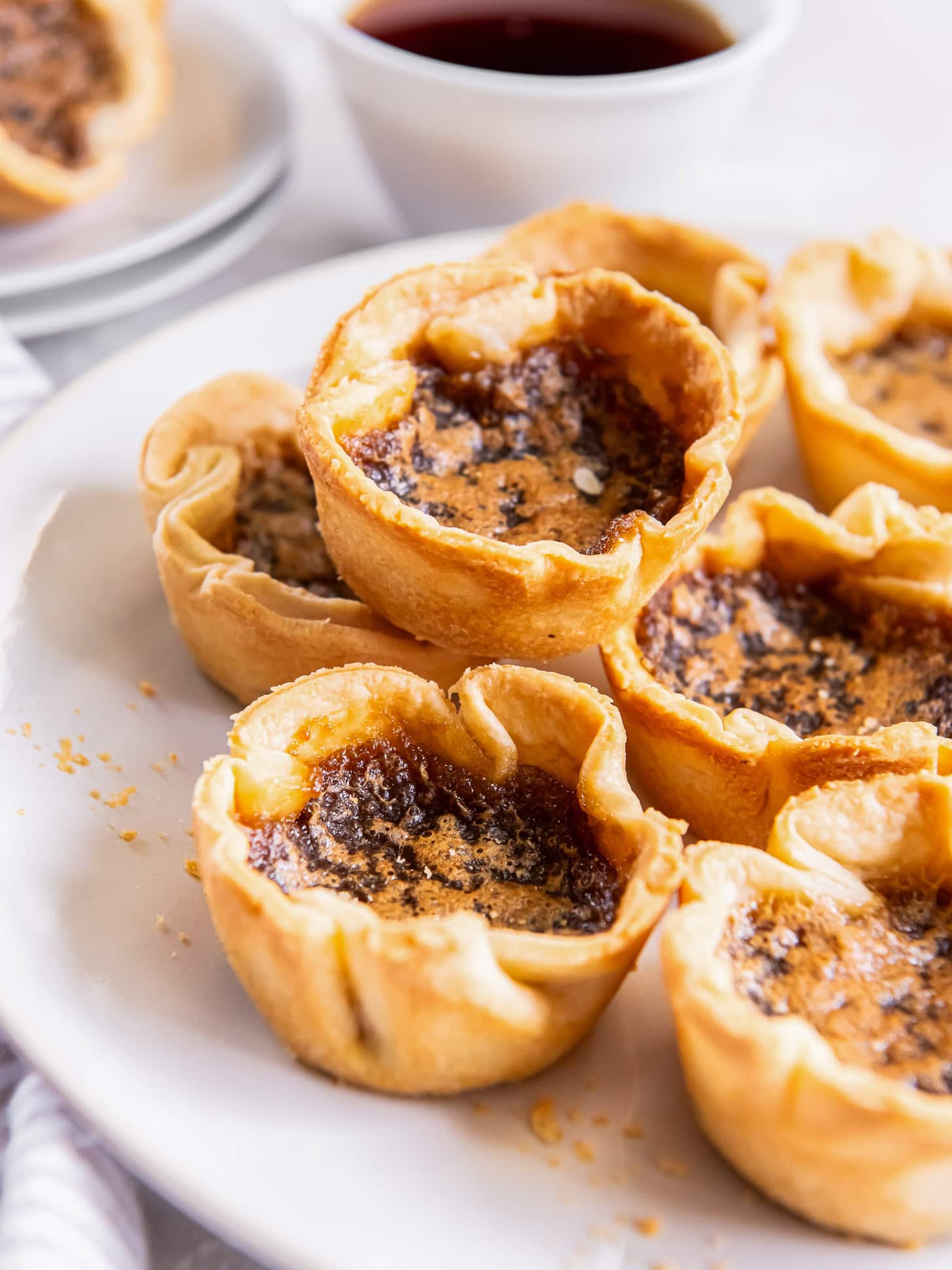 Canadian butter tarts stacked on a white plate served with coffee.