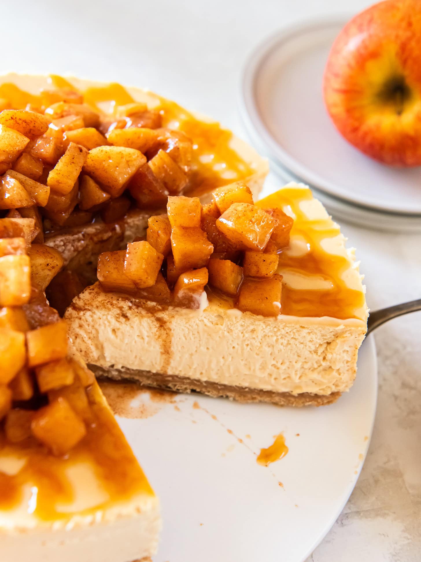Caramel apple cheesecake being served from a white cake plate.