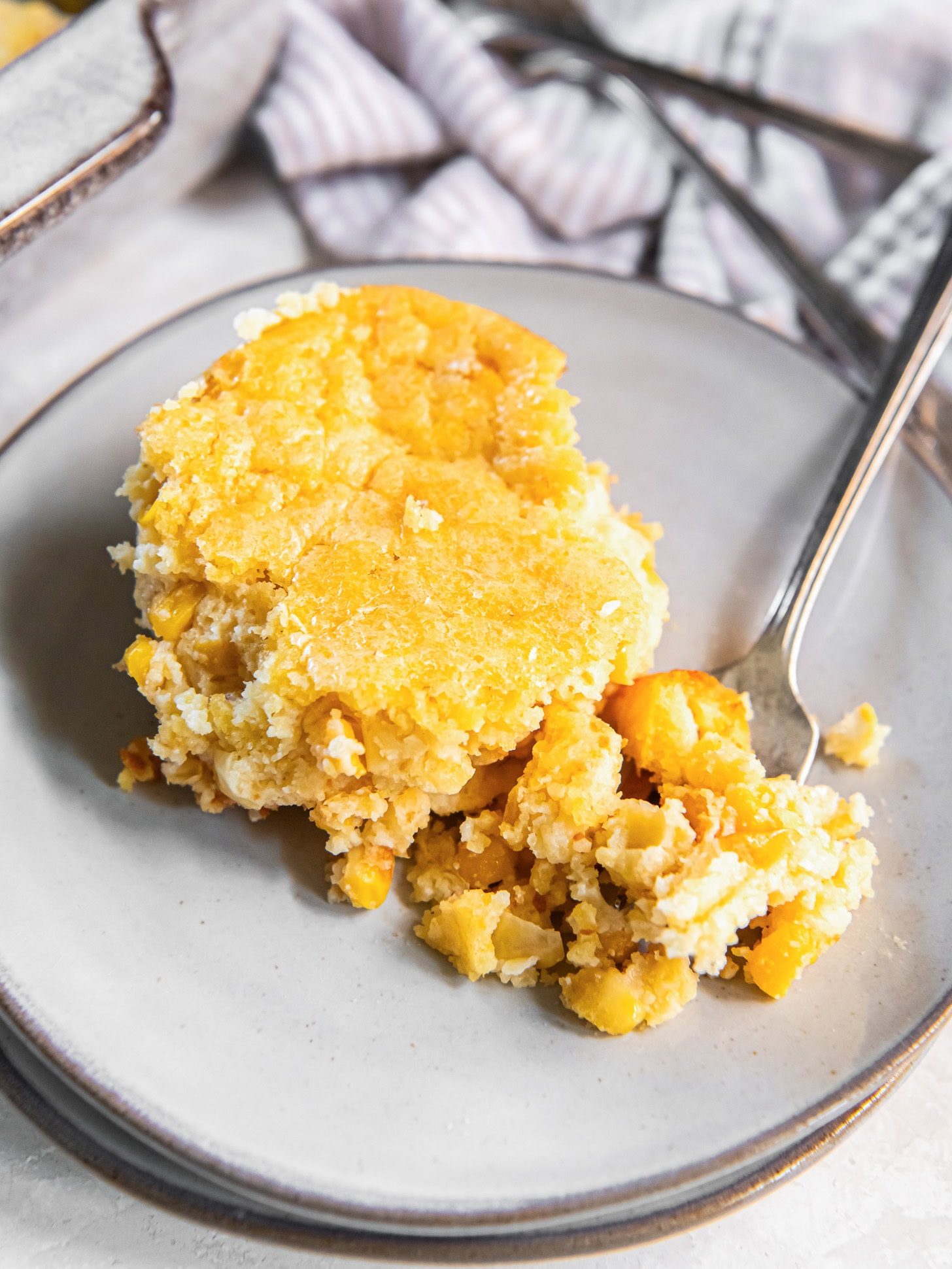 A serving of cornbread pudding with a forkful on a plate.