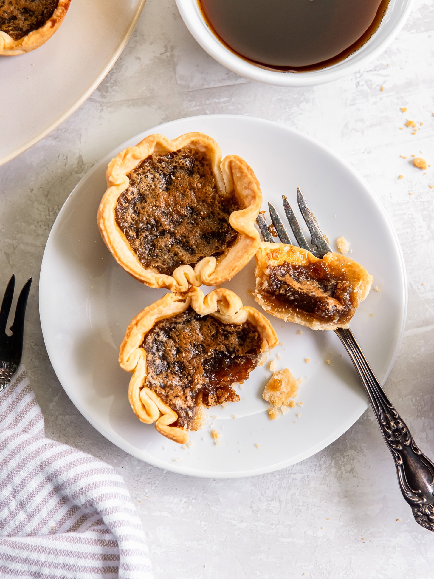 Two butter tarts on a plate with a fork and one cut in half.