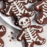 Iced chocolate skeleton cookies on a white plate.