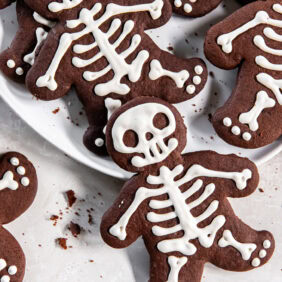 Iced chocolate skeleton cookies on a white plate.