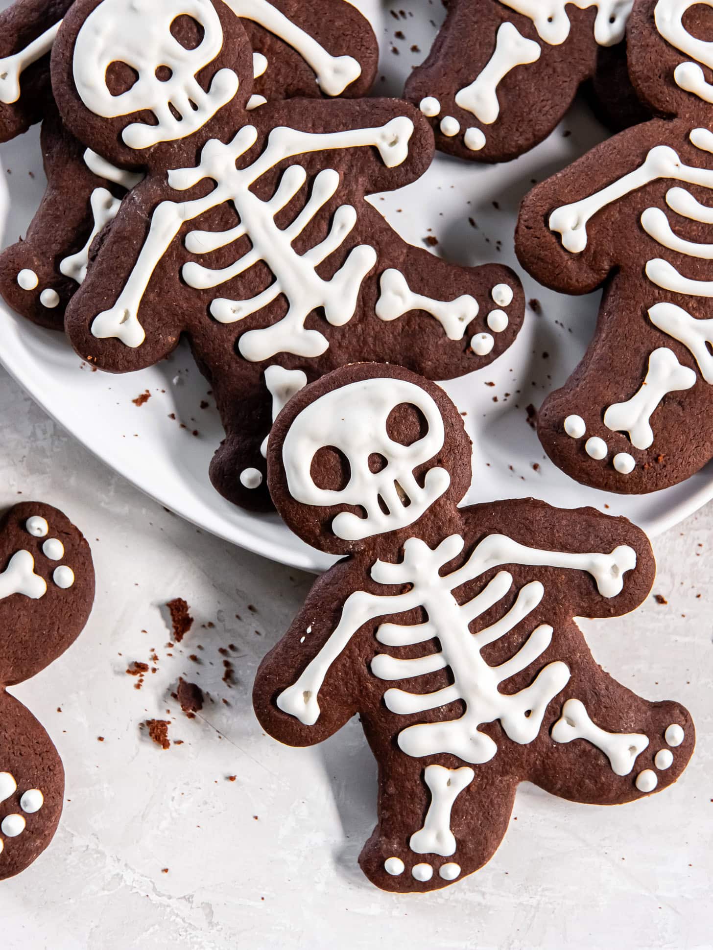 Iced chocolate skeleton cookies on a white plate.