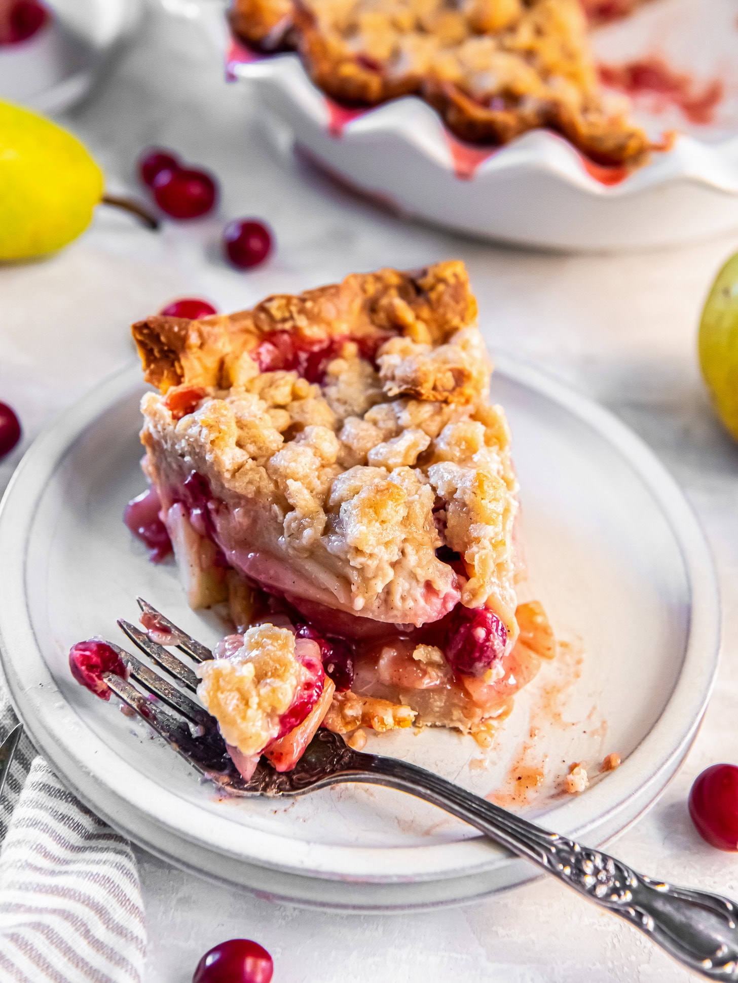 A cut into slice of pear cranberry pie on a plate with a fork.