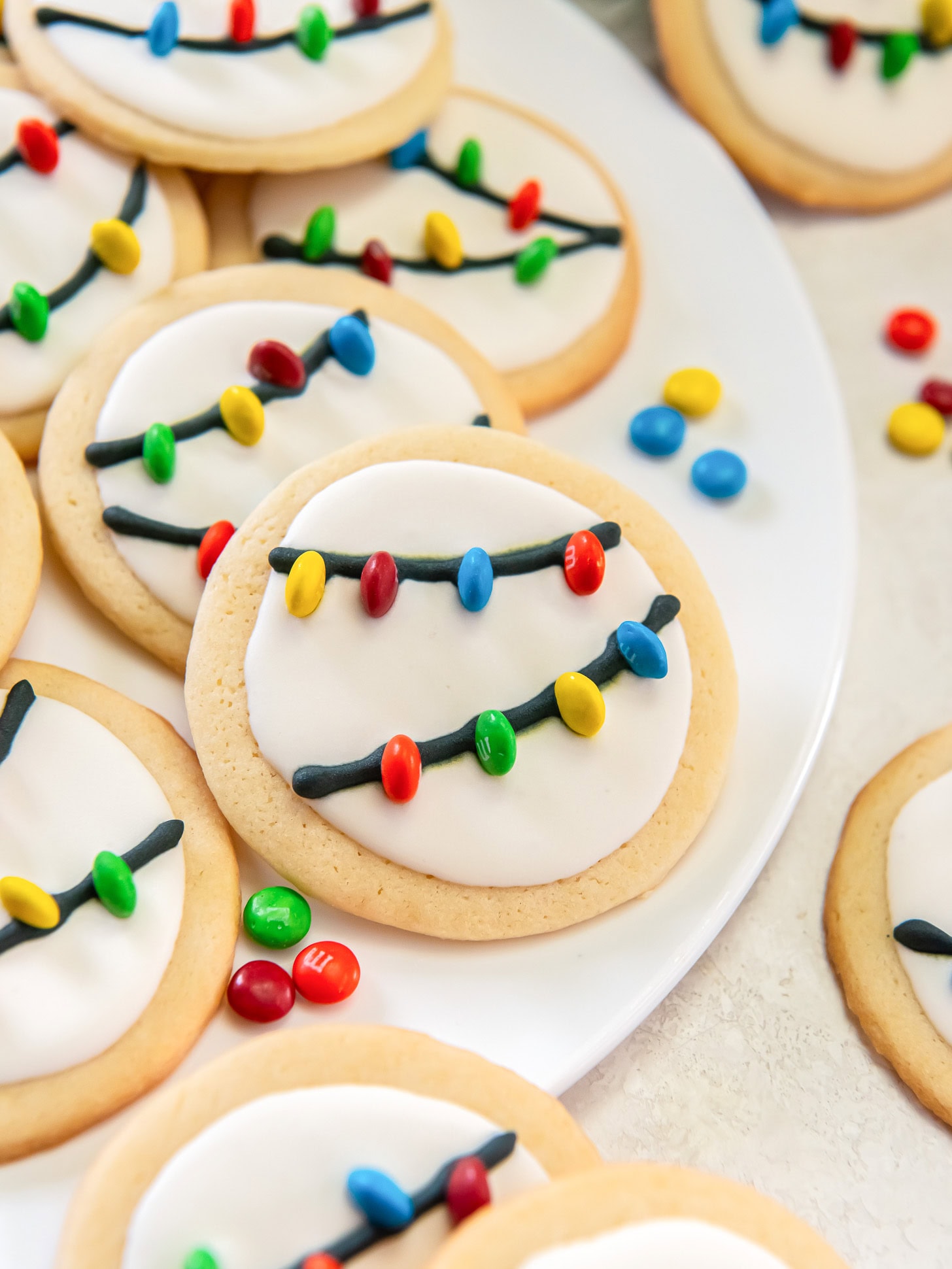 Christmas light sugar cookies on a white plate near mini M&Ms.