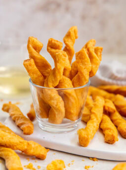 Cheddar cheese straws sticking up out of a small glass.