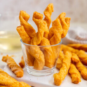 Cheddar cheese straws sticking up out of a small glass.