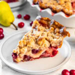 Slice of pear crumble pie with cranberries on a white plate.