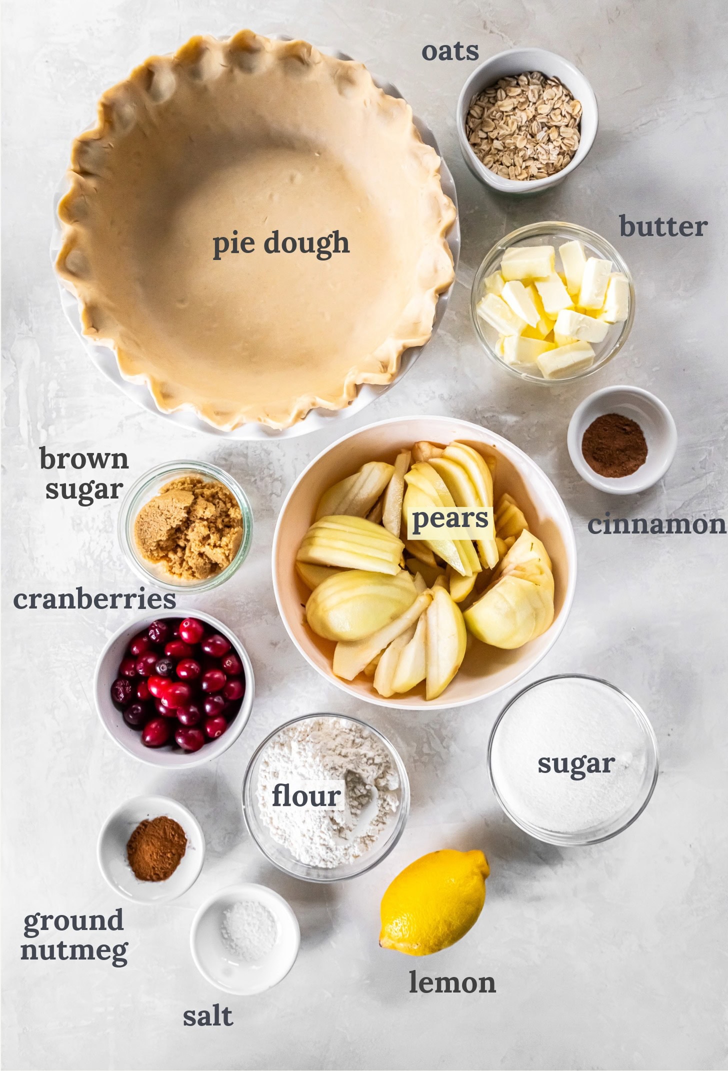Pie dough near bowls of sliced pears, cranberries, butter, sugar and flour.