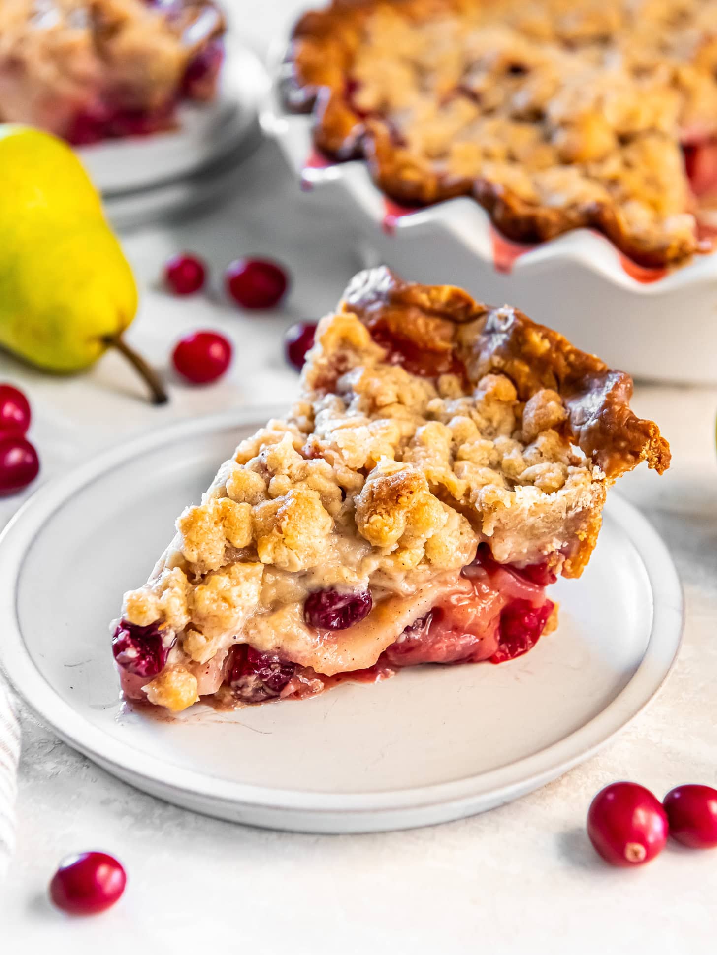 Slice of pear crumble pie with cranberries on a white plate.