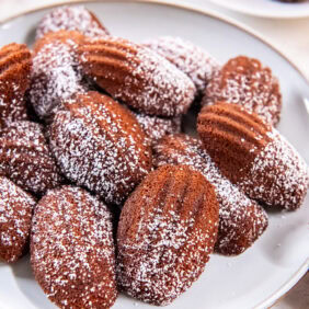Gingerbread Madeleines dusted with powdered sugar on a white plate.