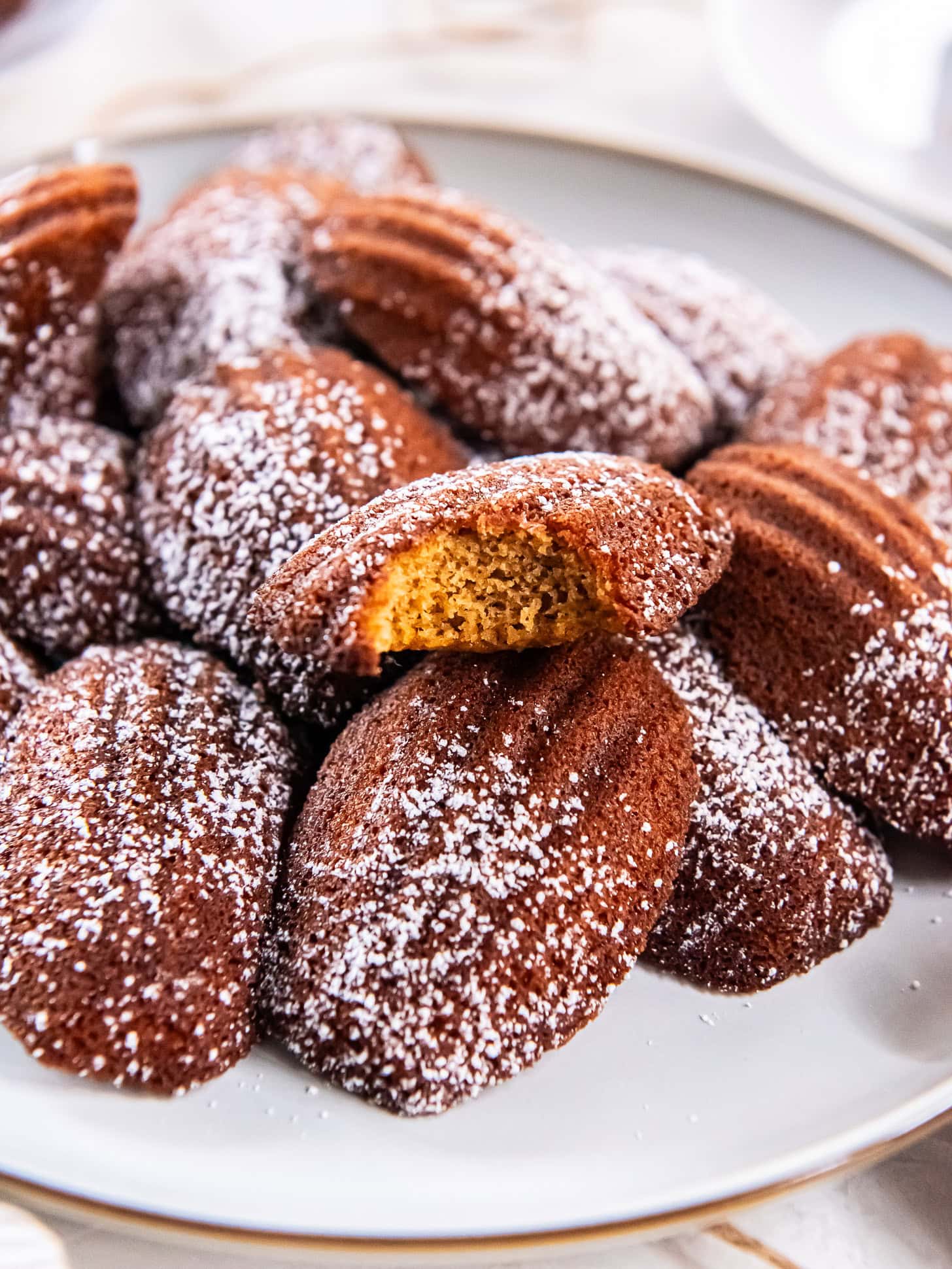 Gingerbread madeleines stacked on a large plate with a bite taken out of one.