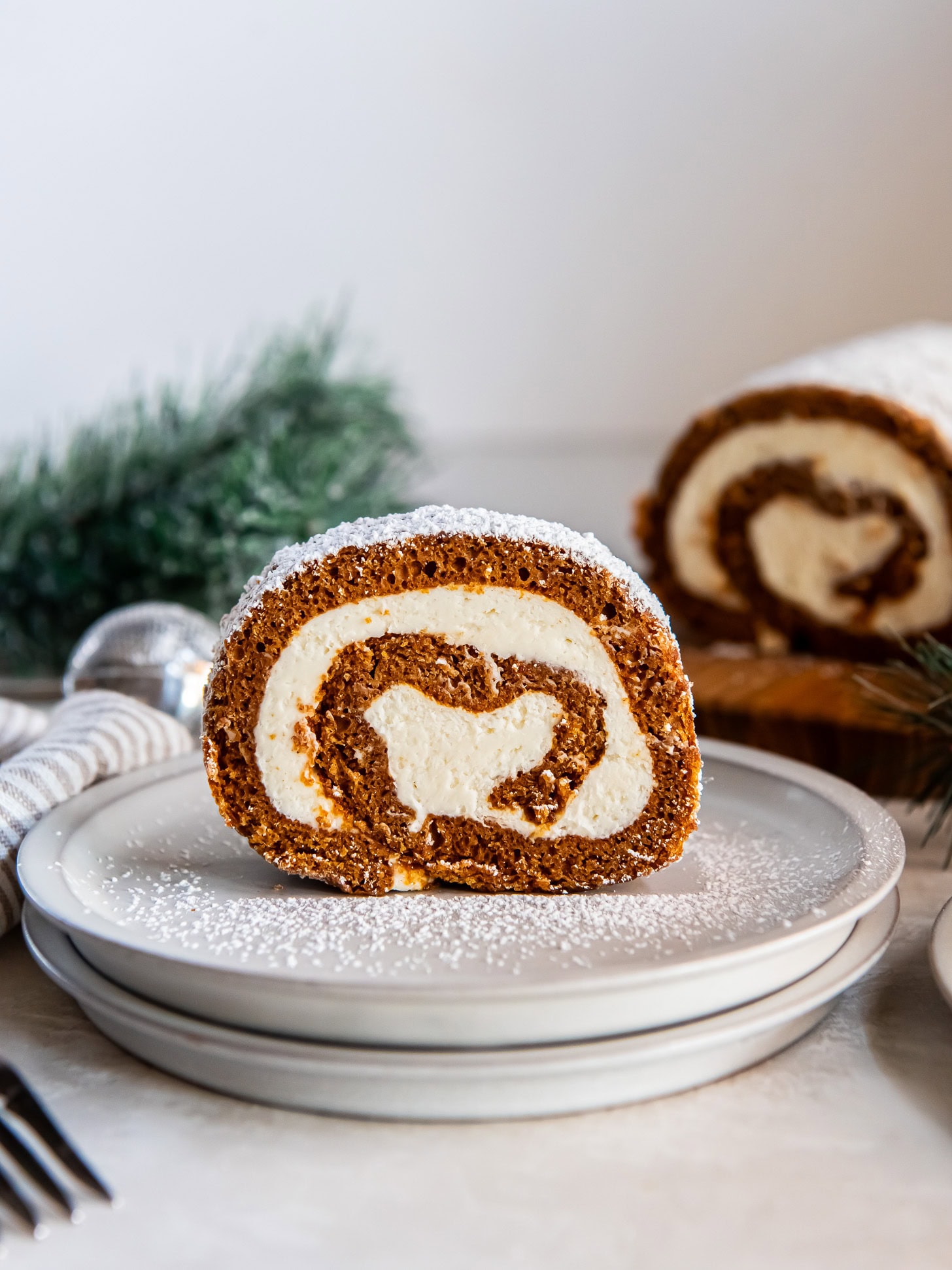 Serving of gingerbread Swiss roll cake dusted with powdered sugar on a white plate.