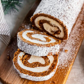 Sliced gingerbread Swiss roll cake on a wooden cutting board.