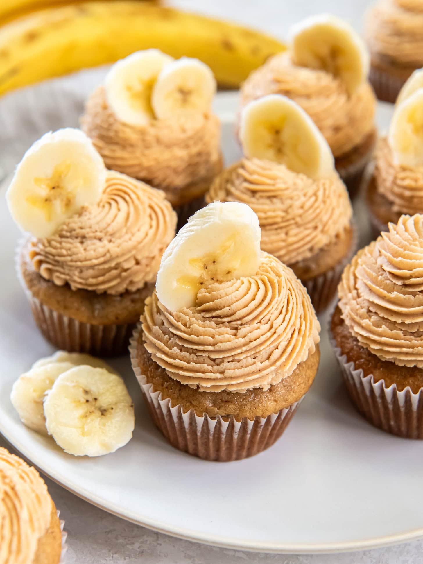 Frosted banana cupcakes with a garnish of a fresh banana slice. 