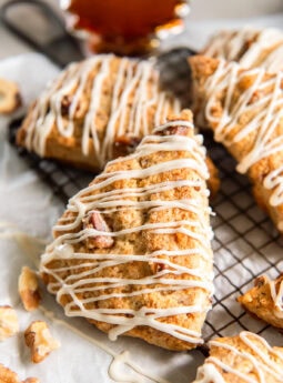 Maple walnut scones drizzled with glaze near a bottle of maple syrup.
