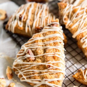 Maple walnut scones drizzled with glaze near a bottle of maple syrup.