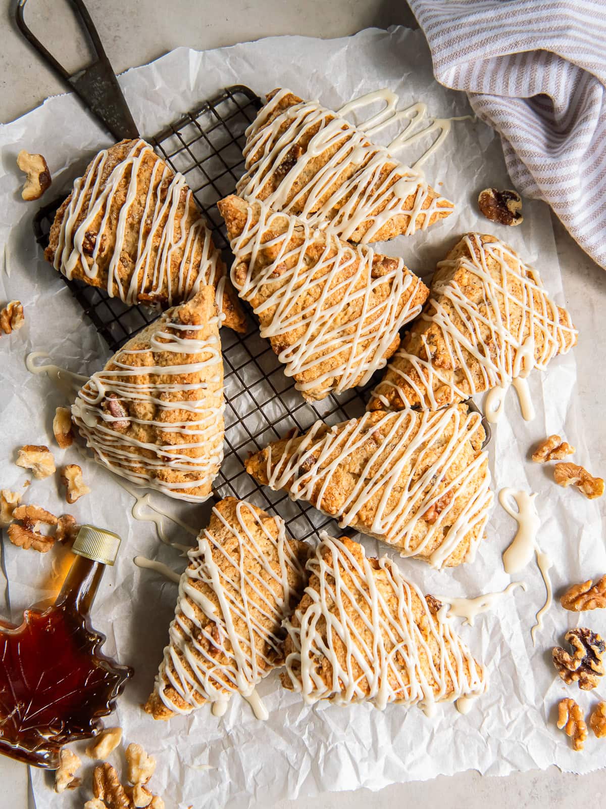 Maple walnut scones drizzled with glaze near a bottle of maple syrup.