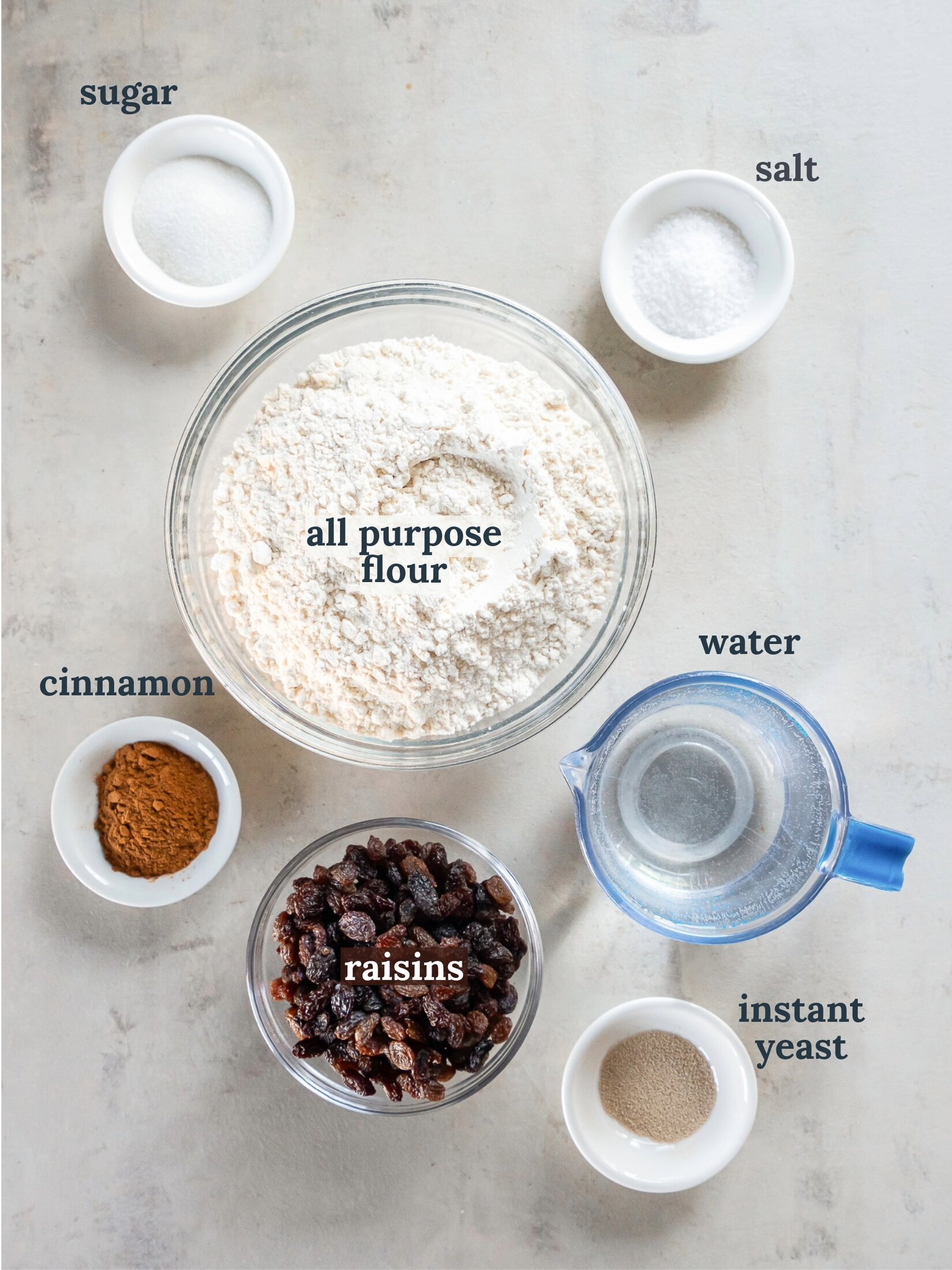 Small bowls with flour, water, yeast, cinnamon and raisins.