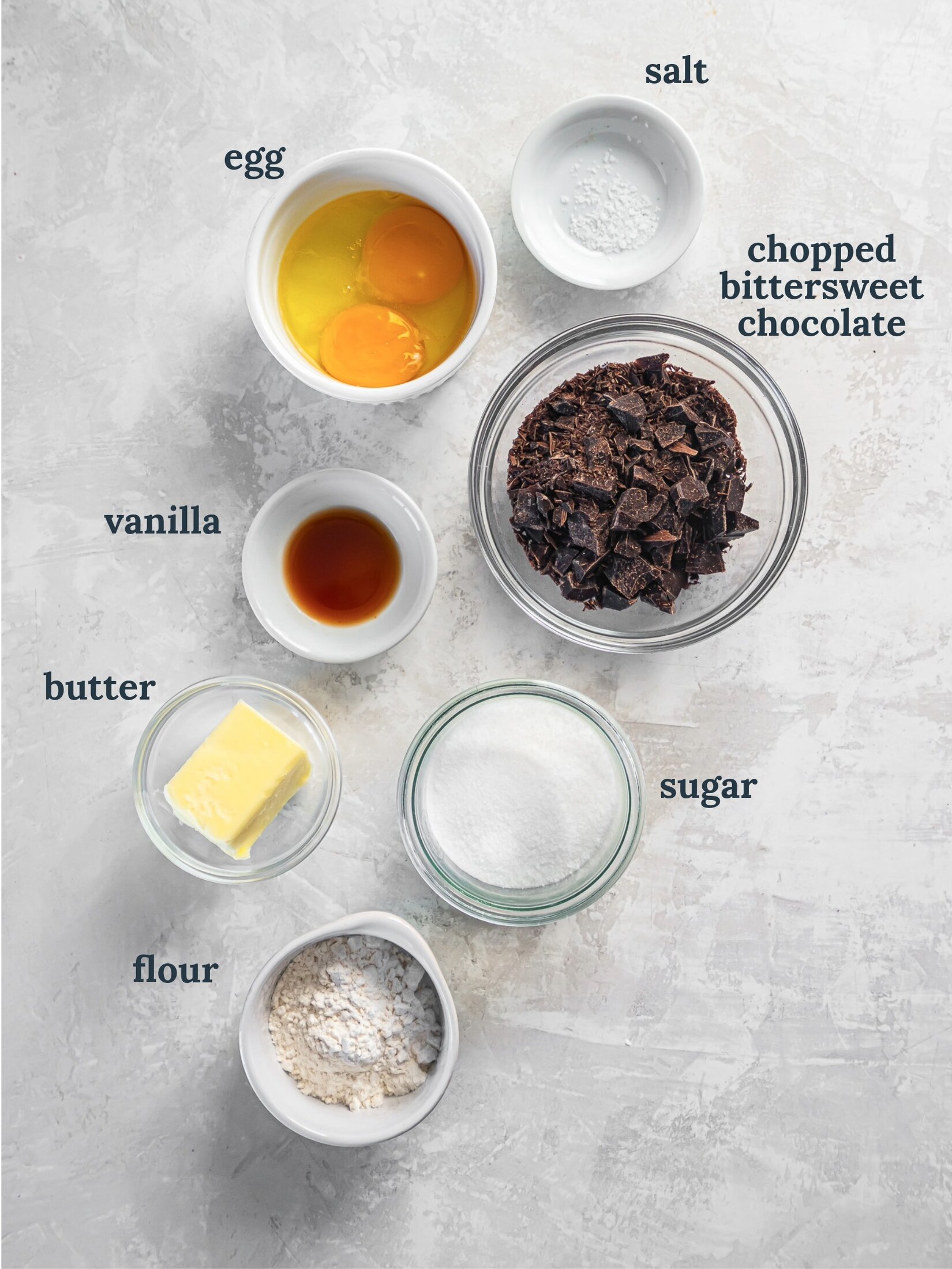 Small bowls with eggs, chocolate, vanilla, sugar, butter and flour.