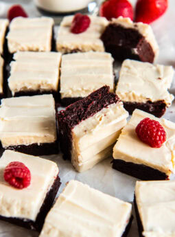 Red velvet cookie bars topped with frosting and fresh raspberries.