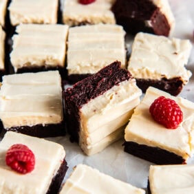 Red velvet cookie bars topped with frosting and fresh raspberries.