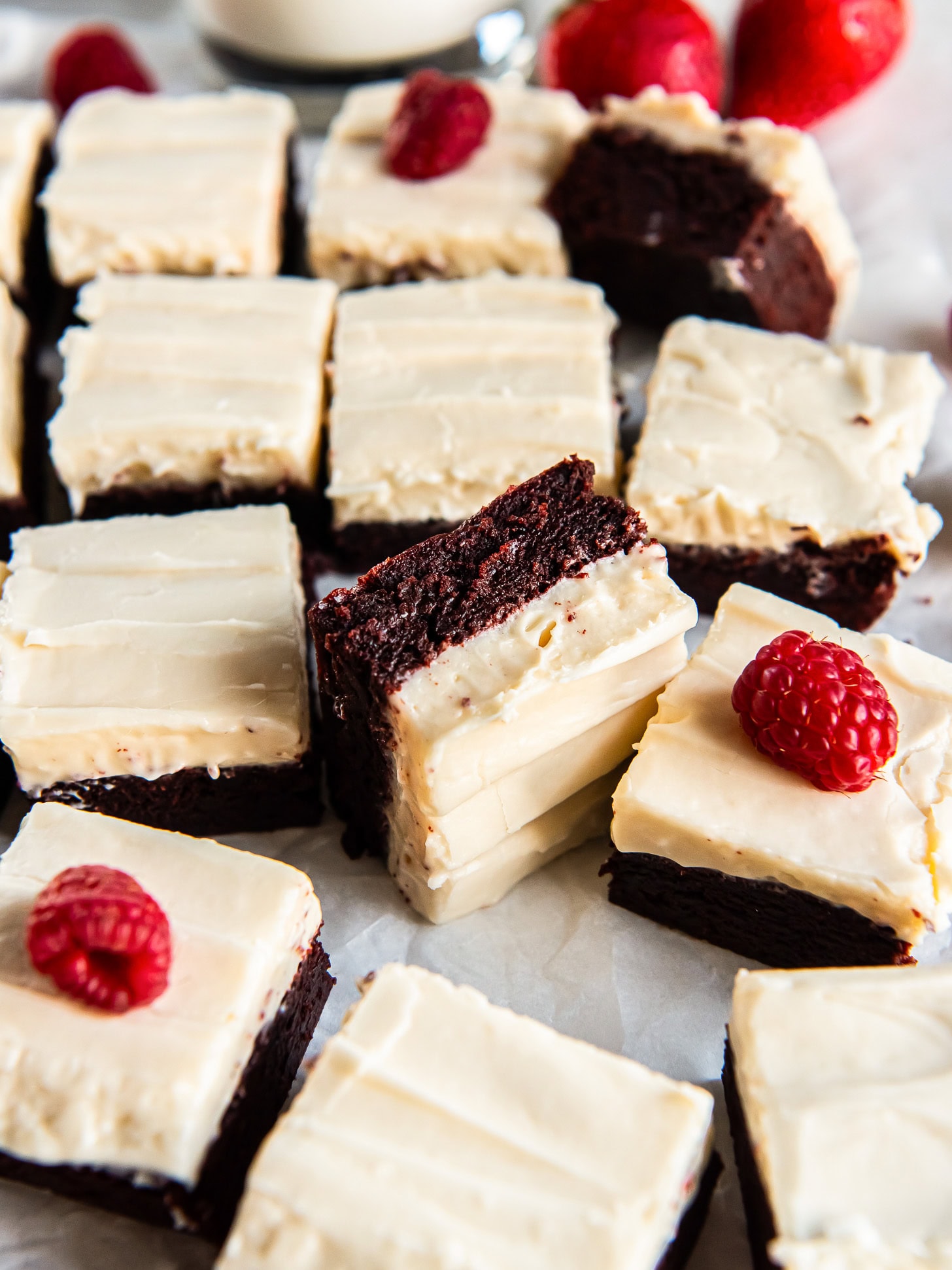 Red velvet cookie bars topped with frosting and fresh raspberries.