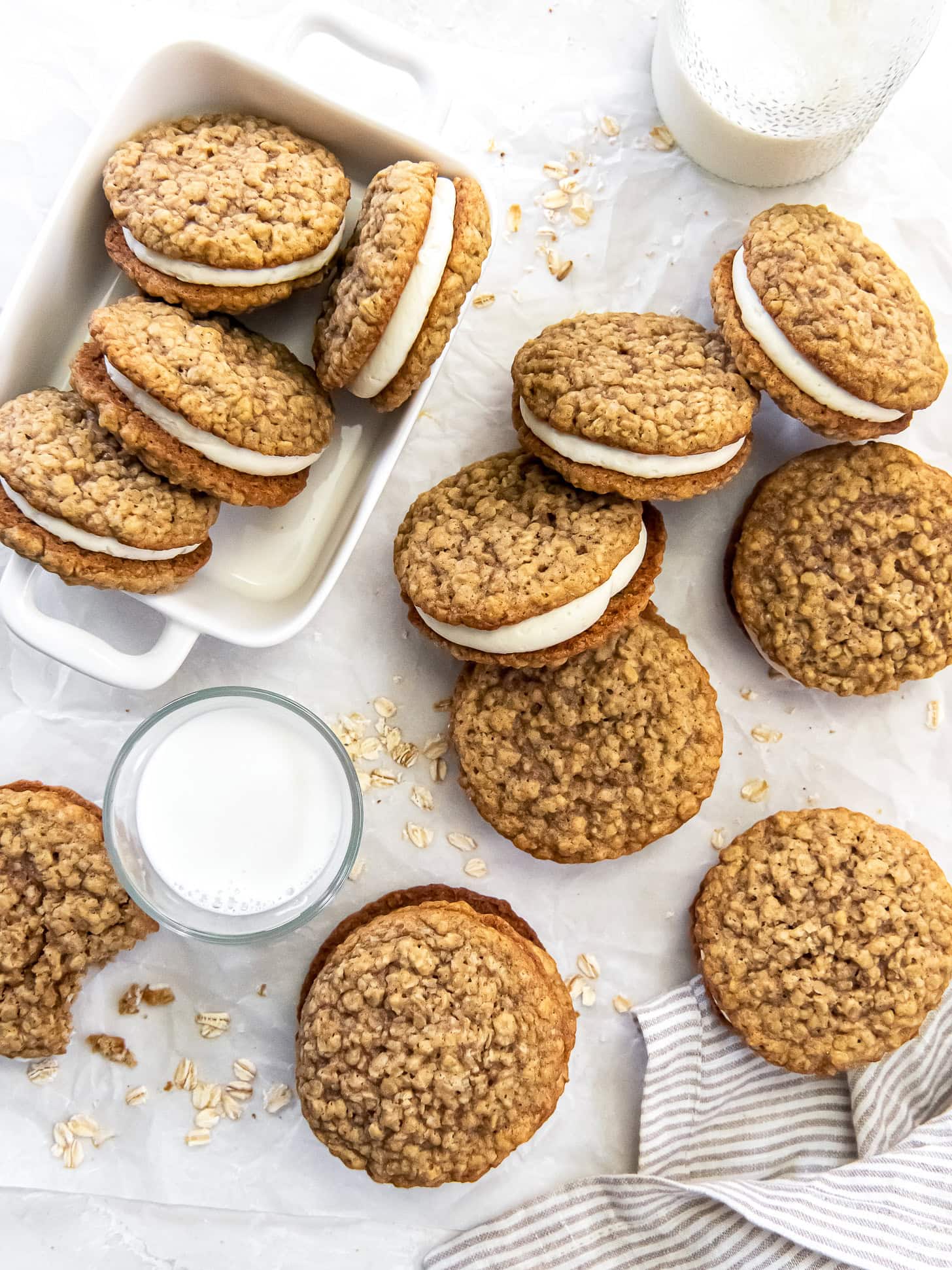 Oatmeal cream pies spread out near milk with some in a white baking dish.