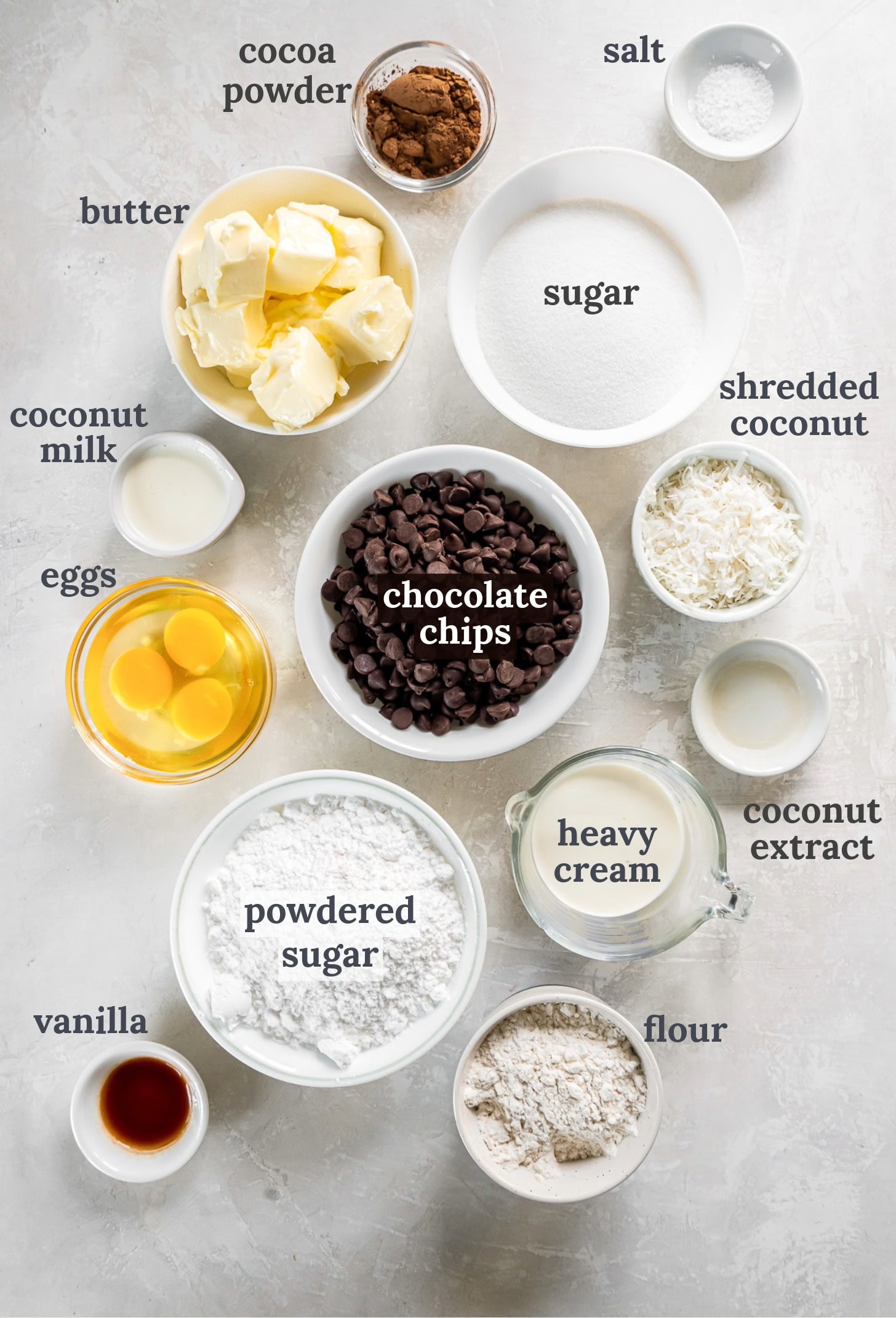 Bowls with chocolate chips, eggs, sugar, flour, buttercream and shredded coconut.