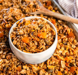 Apricot pistachio granola in a white bowl on a cookie sheet with more granola.