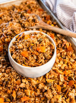Apricot pistachio granola in a white bowl on a cookie sheet with more granola.