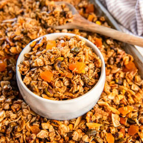 Apricot pistachio granola in a white bowl on a cookie sheet with more granola.