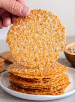 Hand holding up an oatmeal lace cookie from a stack of more cookies.