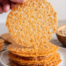 Hand holding up an oatmeal lace cookie from a stack of more cookies.