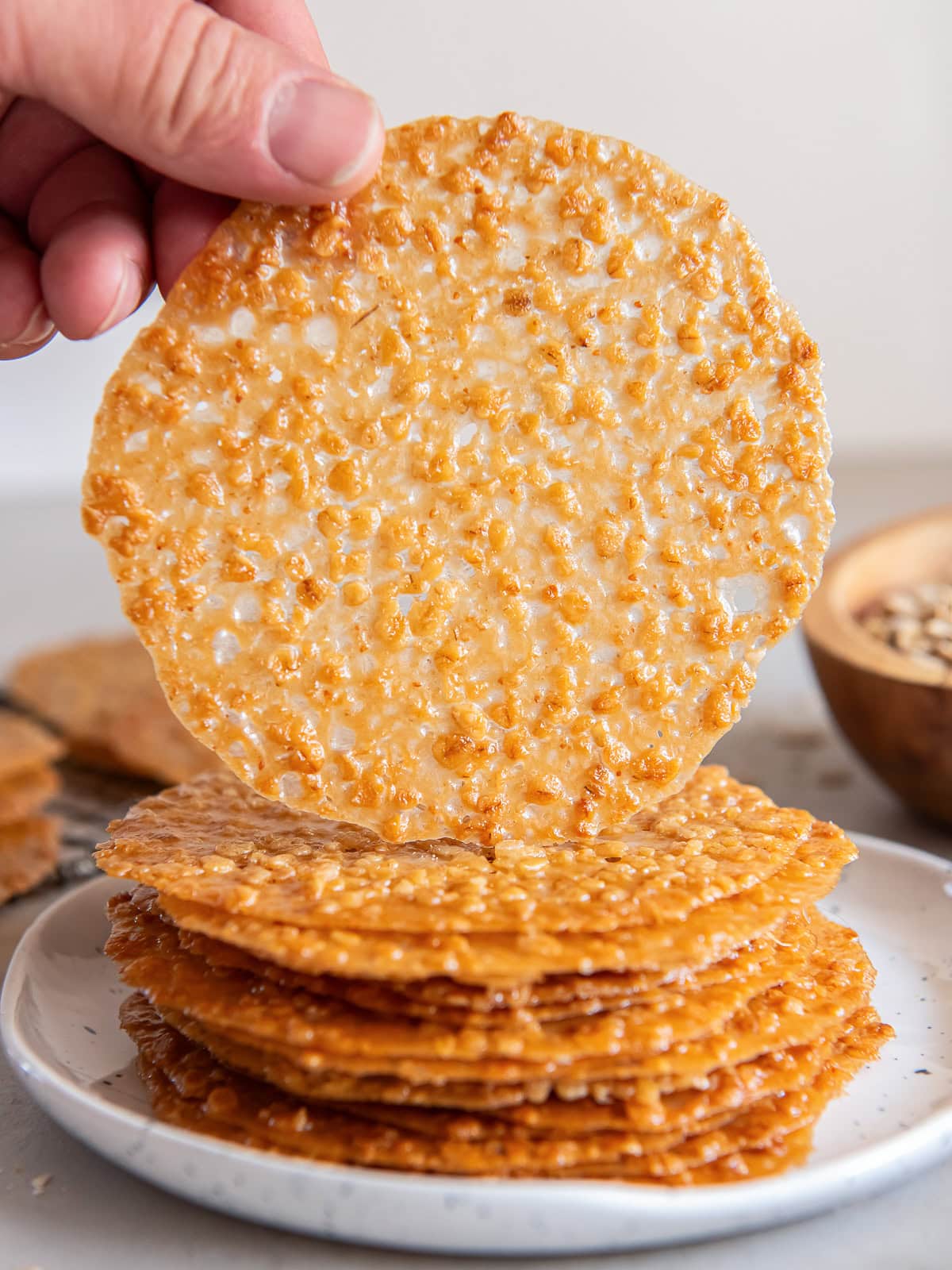 Hand holding up an oatmeal lace cookie from a stack of more cookies.