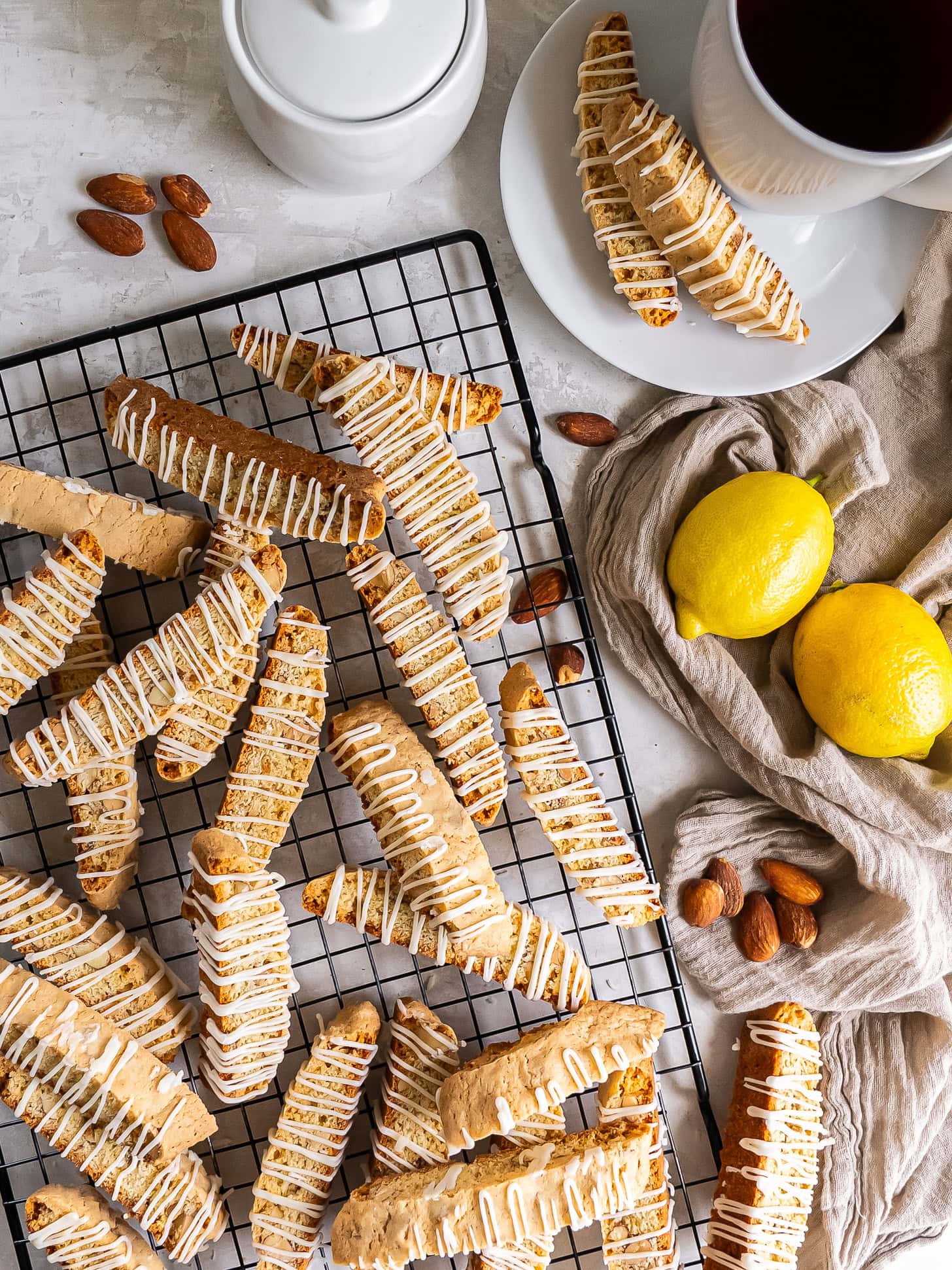 Glazed lemon biscotti on a wire rack near almonds and lemons.