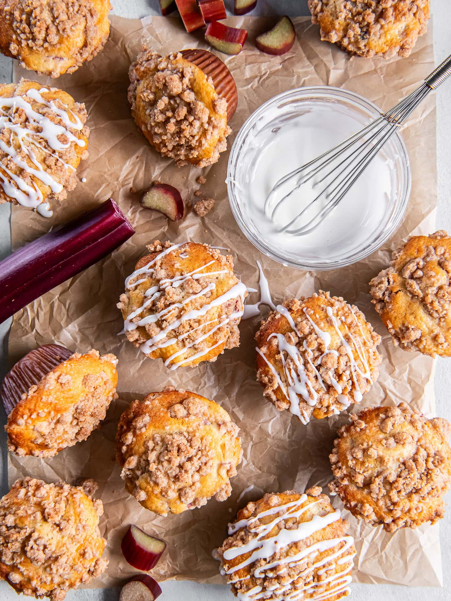 Muffins on parchment being drizzled with lemon glaze.