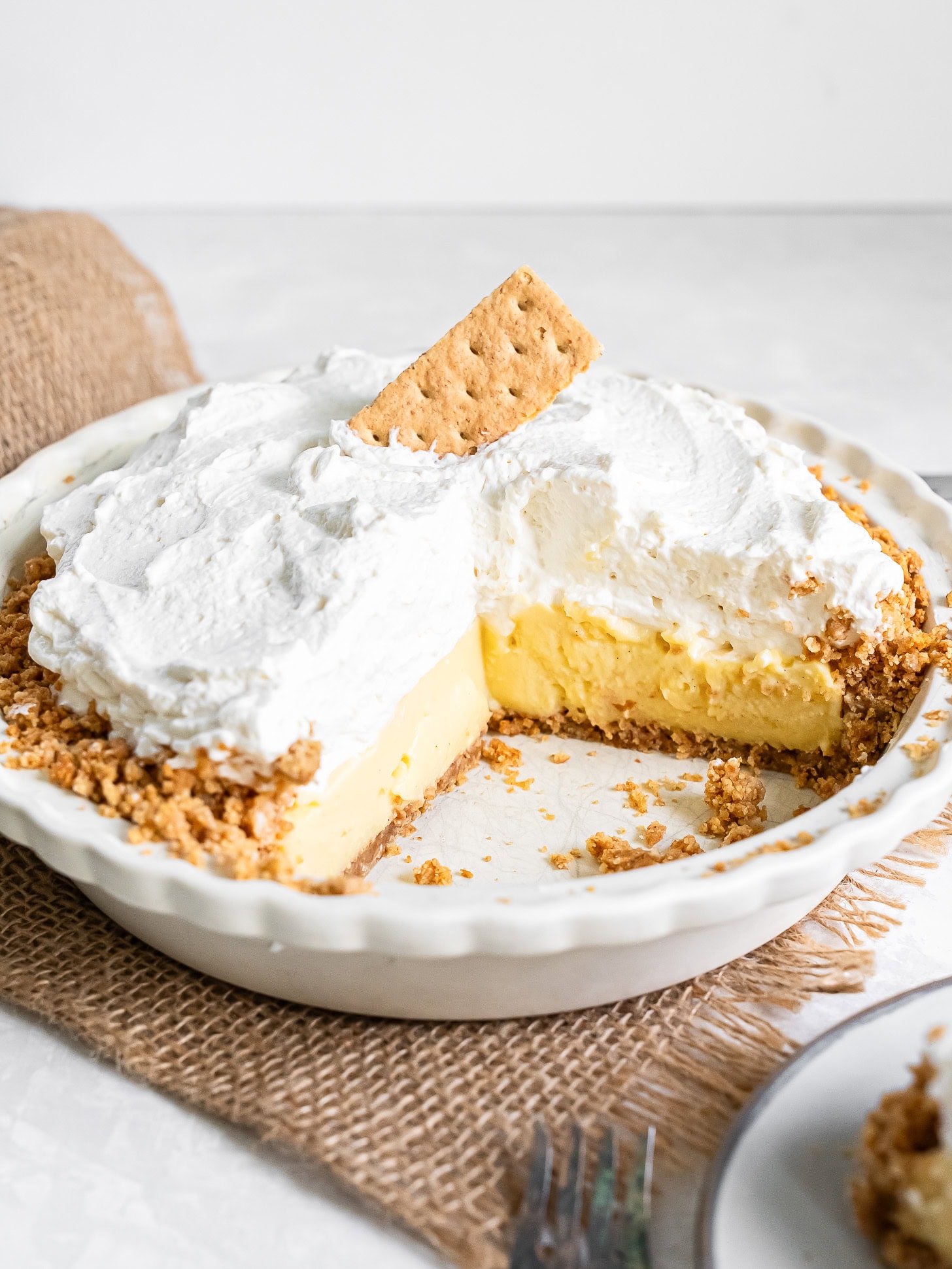A vanilla cream pie garnished with a graham cracker that has a piece removed.